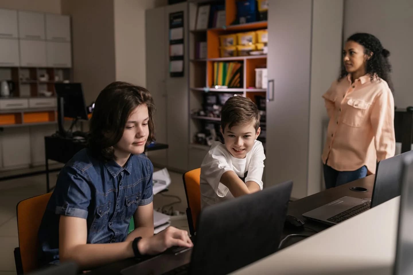 Students working on laptops with a teacher in a classroom